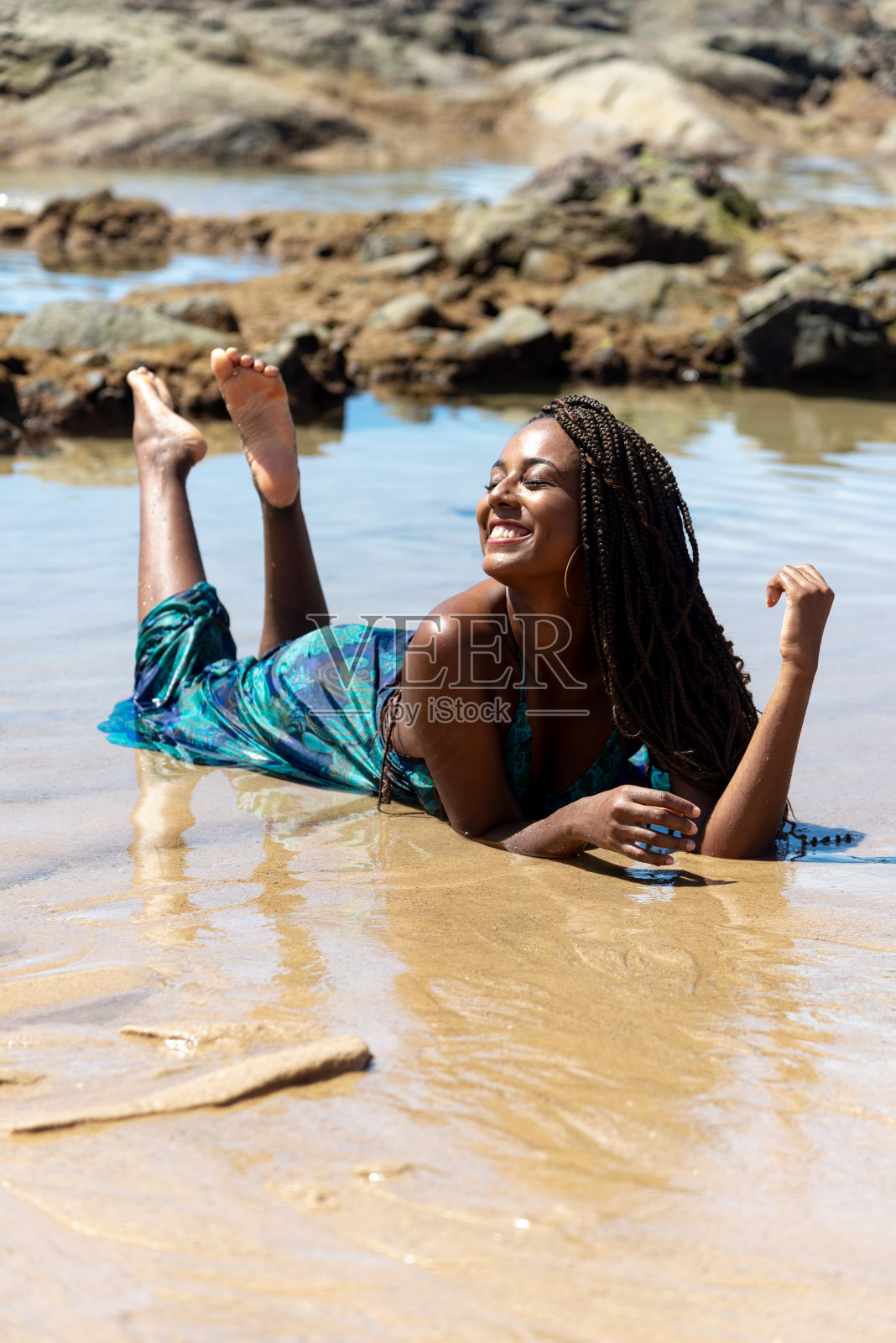 一个梳着辫子、穿着蓝色连衣裙的美女躺在海滩边上摆姿势拍照照片摄影图片