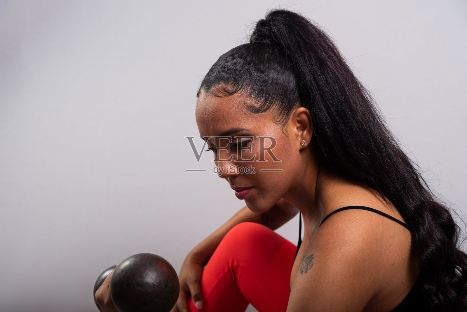 运动员，黑发，快乐和微笑的女人，穿着运动服，坐着做哑铃练习。健康的生活。照片摄影图片