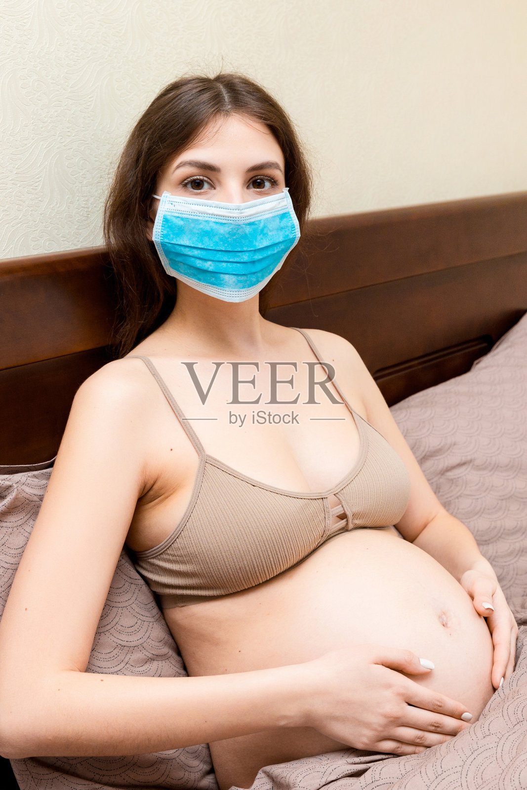 戴医用防护口罩的孕妇感染了冠状病毒，正在卧床休息。防止感染胎儿。全球流行。保持隔离概念照片摄影图片