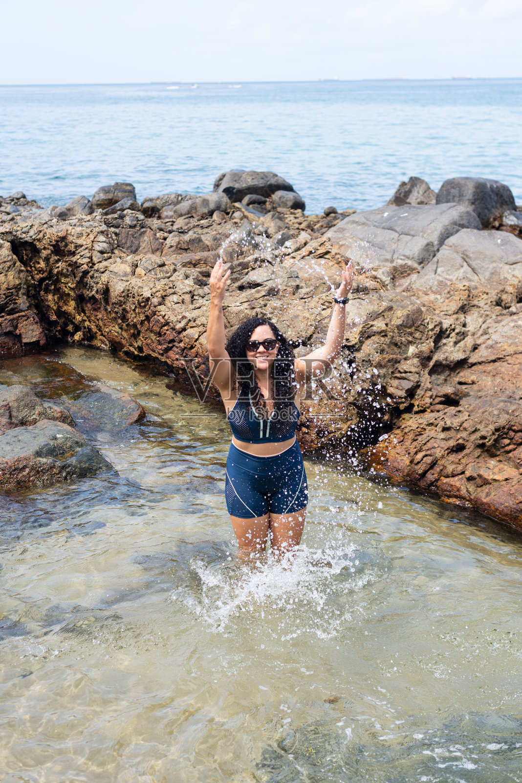美女站在沙滩上的水坑里，向空中泼水。照片摄影图片