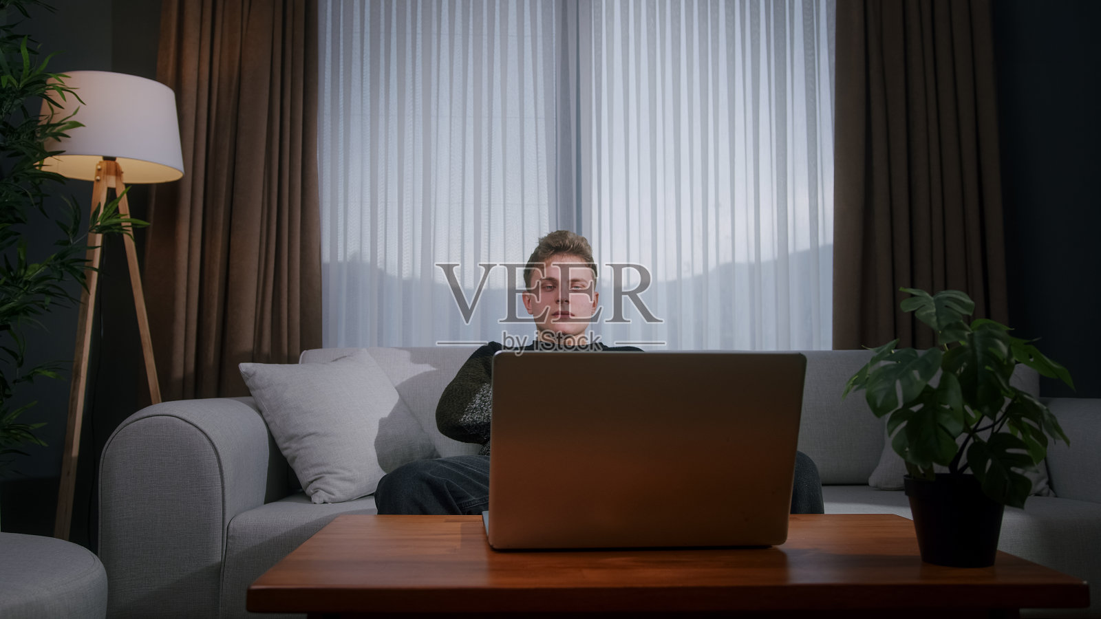 在家使用笔记本电脑时感到焦虑和压力的悲伤年轻人。对笔记本电脑上的损失和坏消息做出反应的沮丧年轻人照片摄影图片