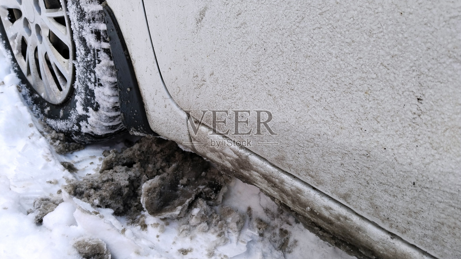 车轮踩在脏兮兮的雪地上。冬季道路上的泥土、盐和化学品。城市生态。保护和清洗汽车。开车。汽车轮毂罩。轮胎压力。轮胎的变化。环境污染概念。照片摄影图片