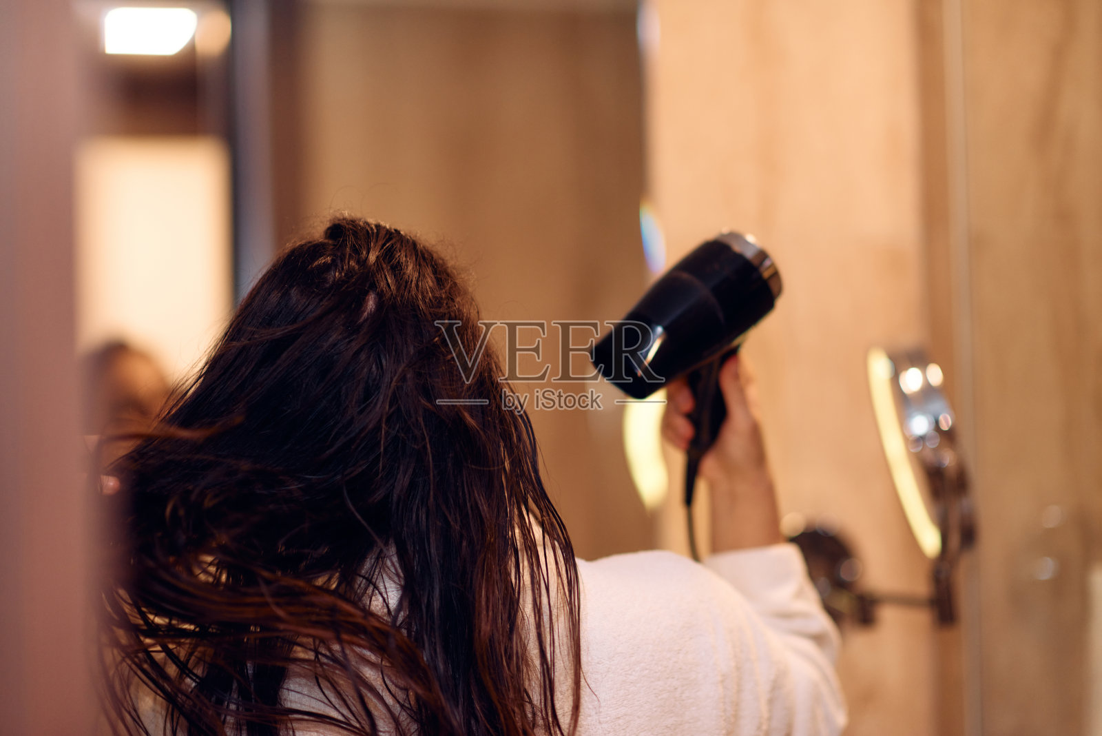 沐浴后，一个快乐的女人戴着耳机，在浴室里用吹风机吹干头发，这是一个无忧无虑、充满活力的自我护理和放松时刻照片摄影图片