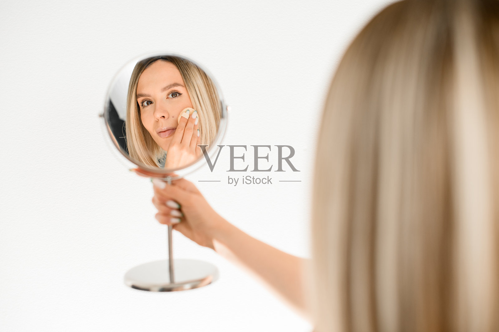 一个手里拿着海绵的美丽女人看着镜子里的自己照片摄影图片