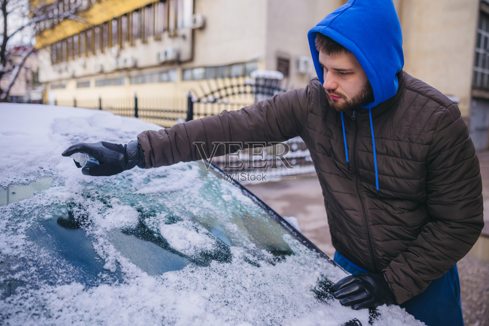 一名年轻人正在使用除冰喷雾清除汽车挡风玻璃上的冰照片摄影图片