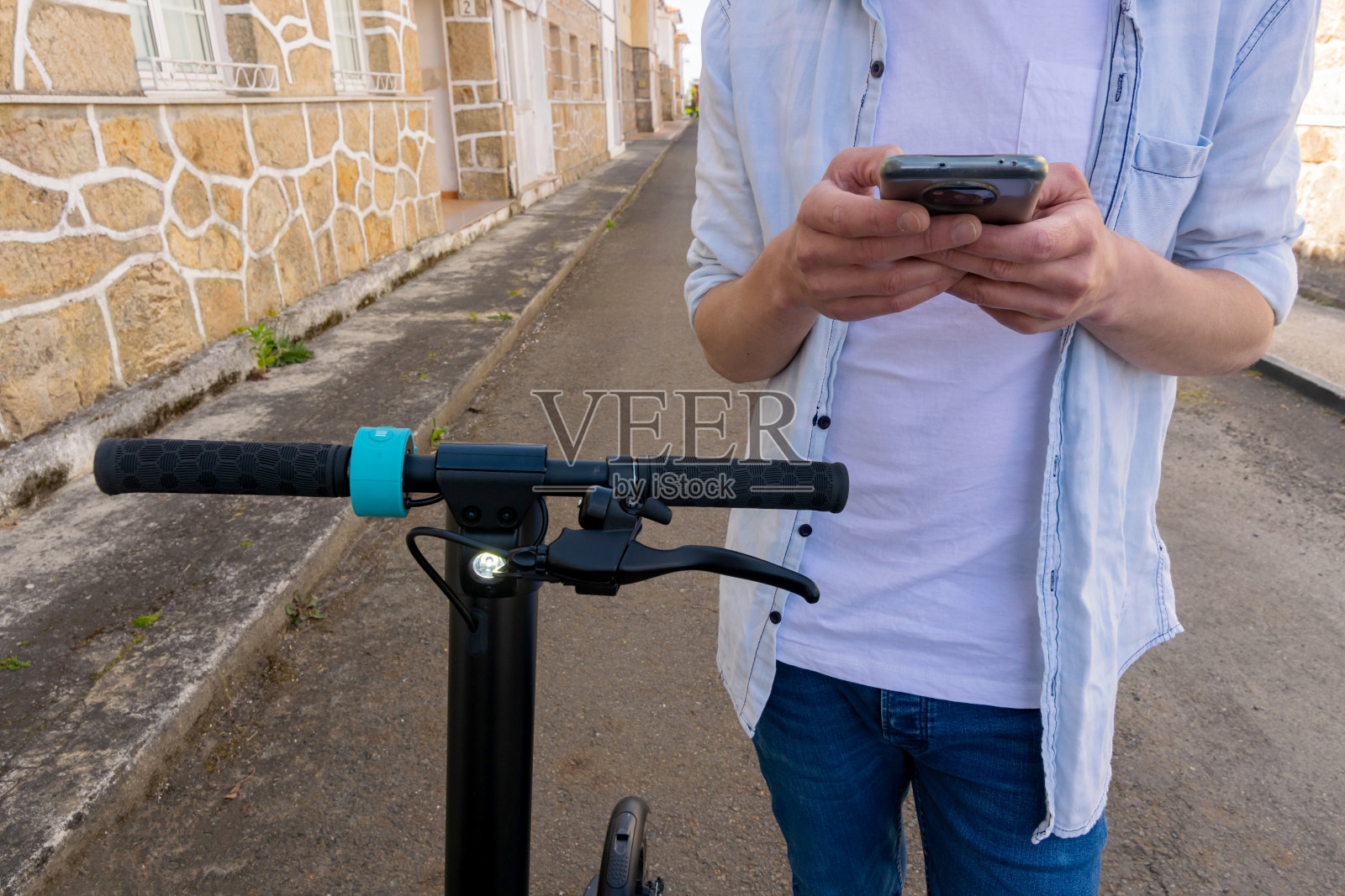 一个年轻人看着他的电动滑板车旁边的智能手机照片摄影图片