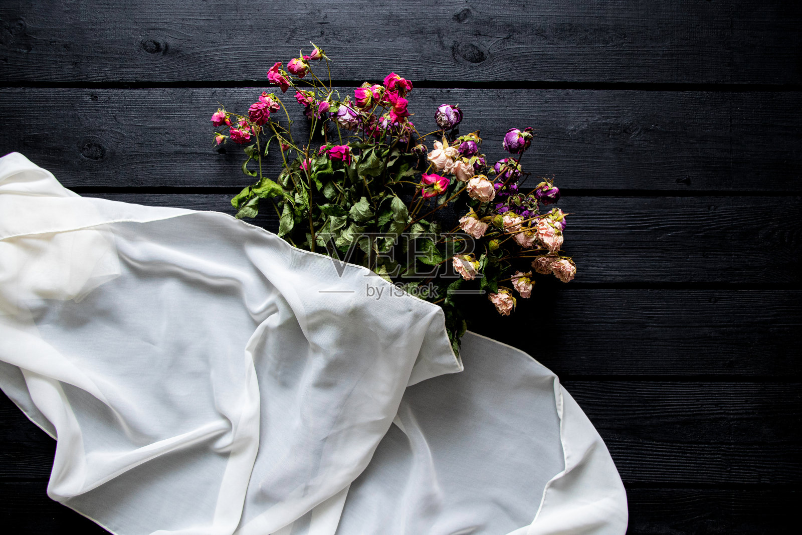 一束干玫瑰和一条白围巾躺在一个黑色的木板上，一束干花照片摄影图片