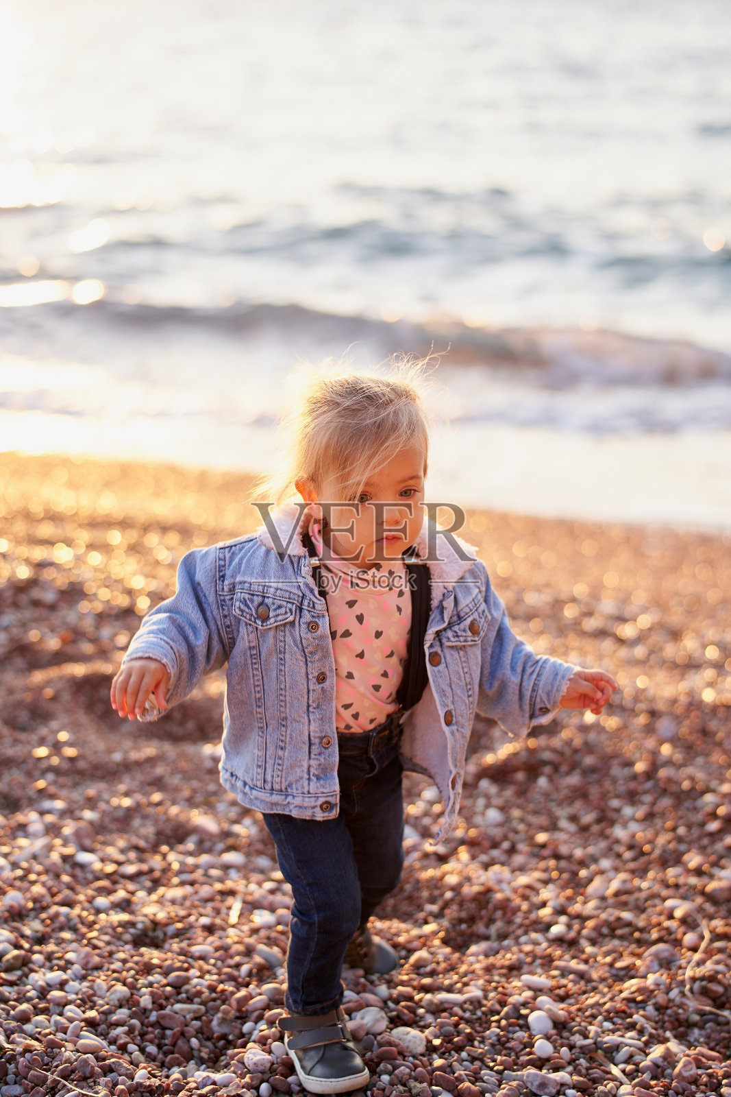 穿着夹克的小女孩走在卵石沙滩上照片摄影图片