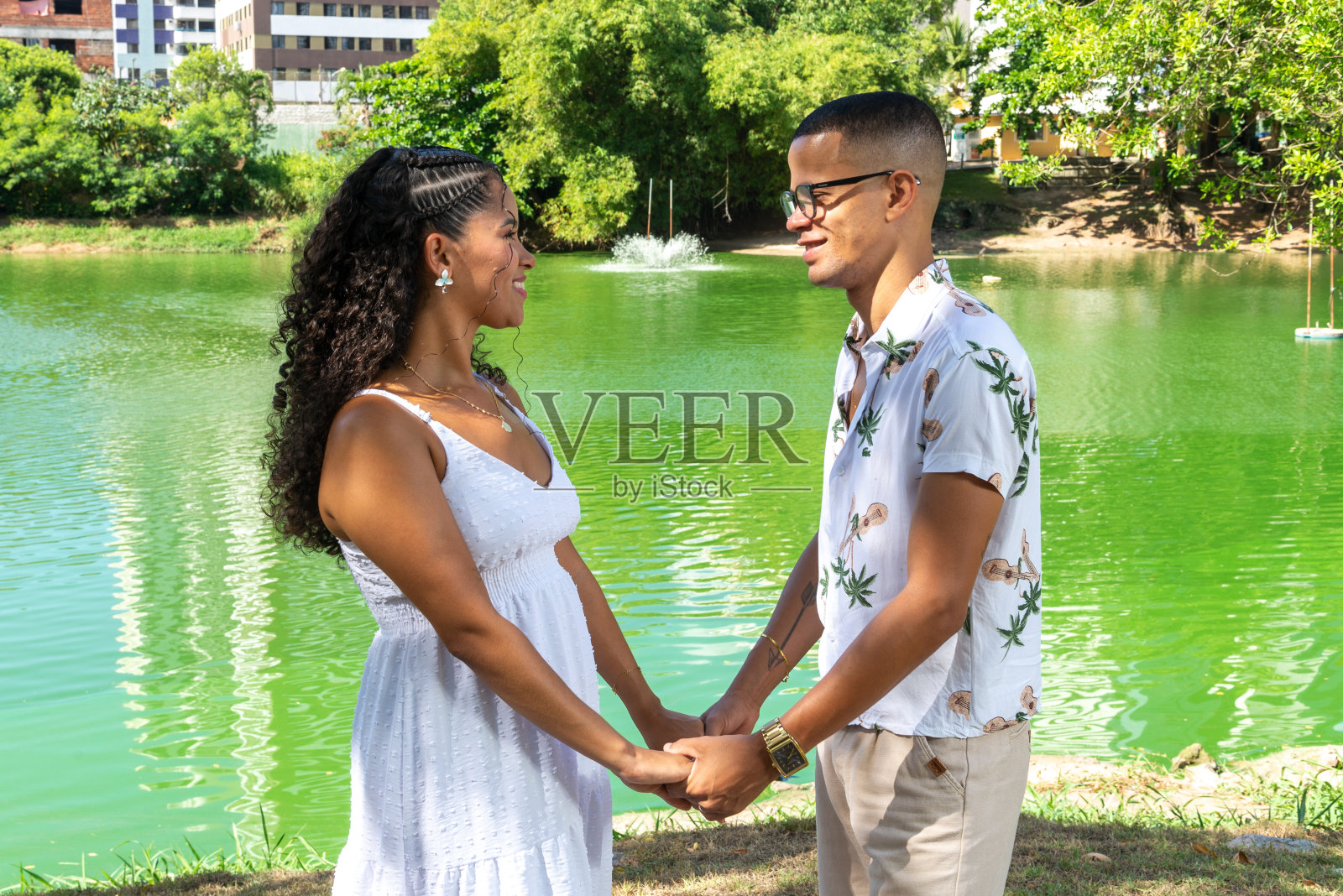 年轻情侣手牵着手，互相对望，背景是绿色泻湖，女子已怀孕照片摄影图片