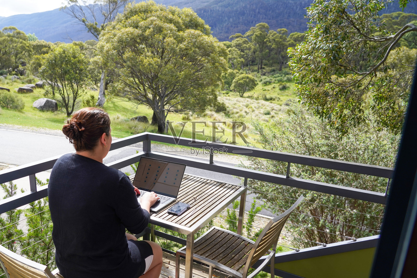 一个女人在阳台上远程工作，俯瞰着丛林和山脉照片摄影图片