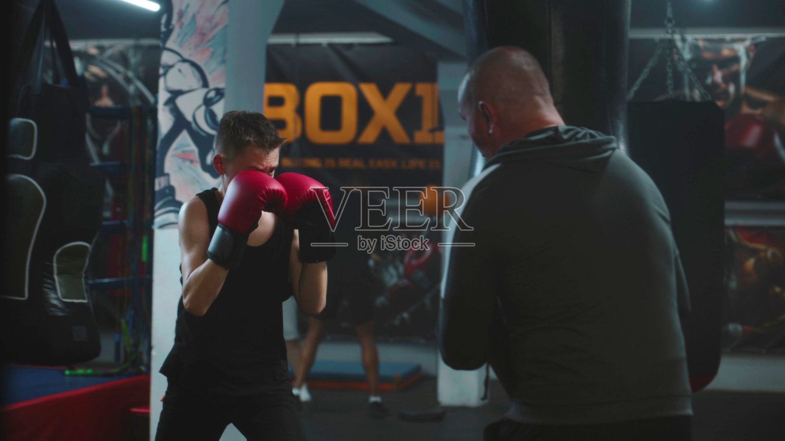 戴着拳击手套的年轻拳击手在黑暗的体育馆里与教练一起练习照片摄影图片