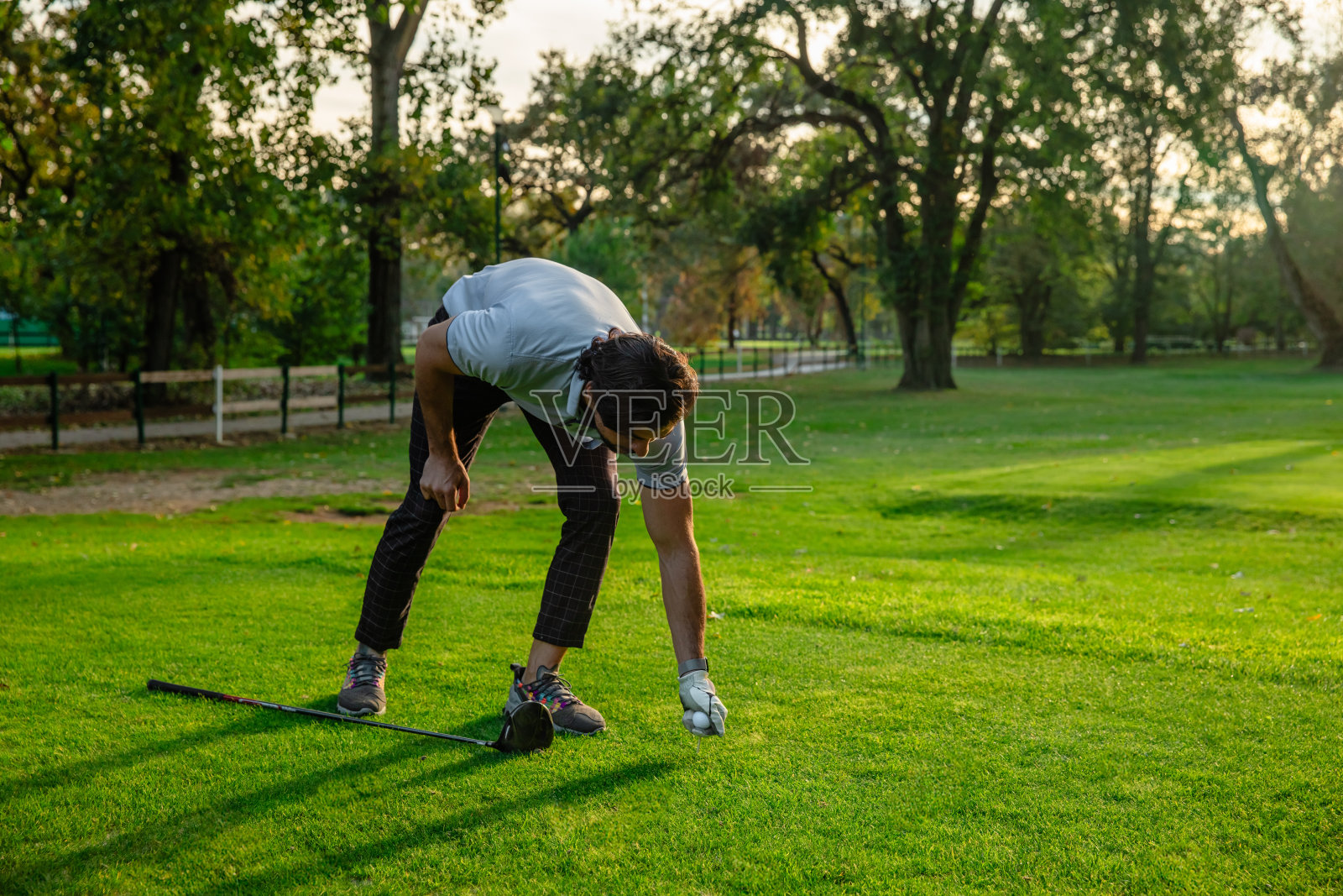 一个高尔夫球手准备打击一个高尔夫球在一个阳光明媚的日子在高尔夫球场-股票照片照片摄影图片