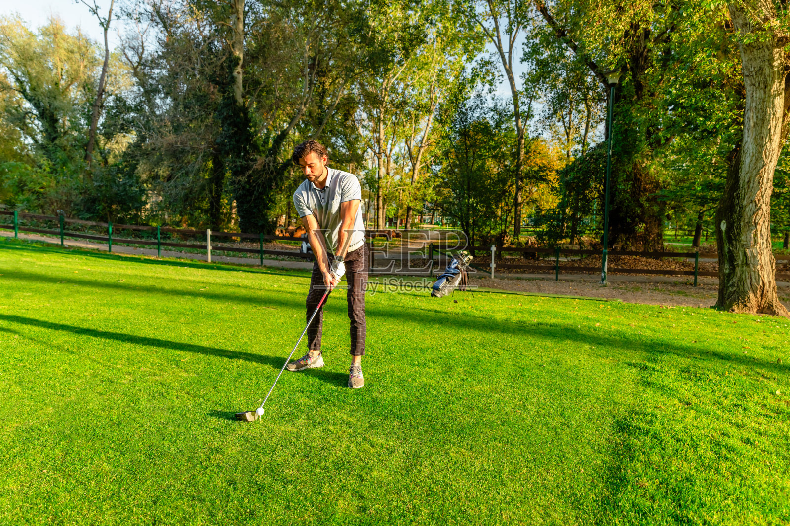 一个高尔夫球手准备打击一个高尔夫球在一个阳光明媚的日子在高尔夫球场-股票照片照片摄影图片