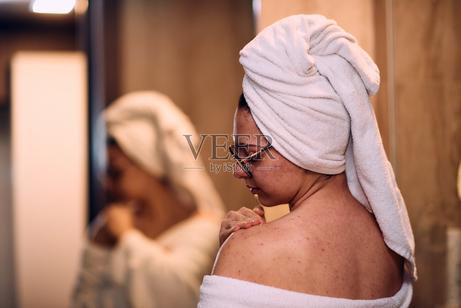 一个女人在放松的沐浴后优雅地将滋润的保湿霜涂抹在她的肩膀上，体现了一个容光焕发和恢复活力的护肤程序照片摄影图片