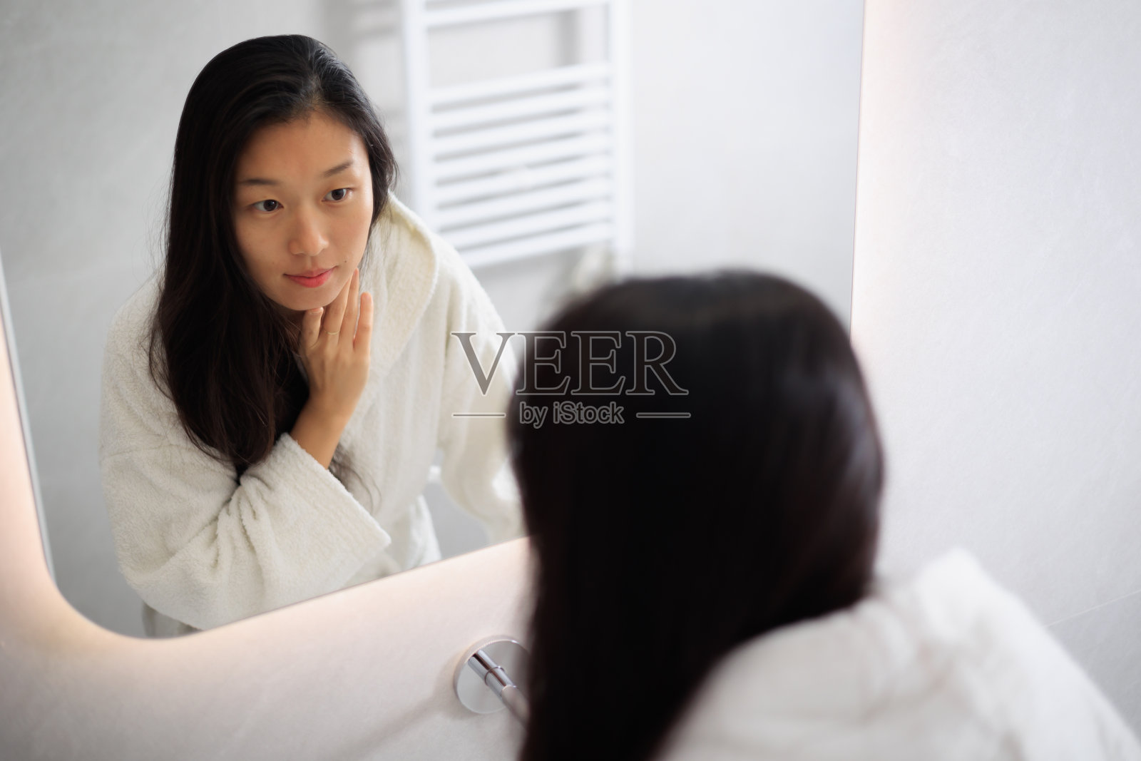 美丽的年轻亚洲女人看着她在镜子里，照顾她的皮肤和头发照片摄影图片