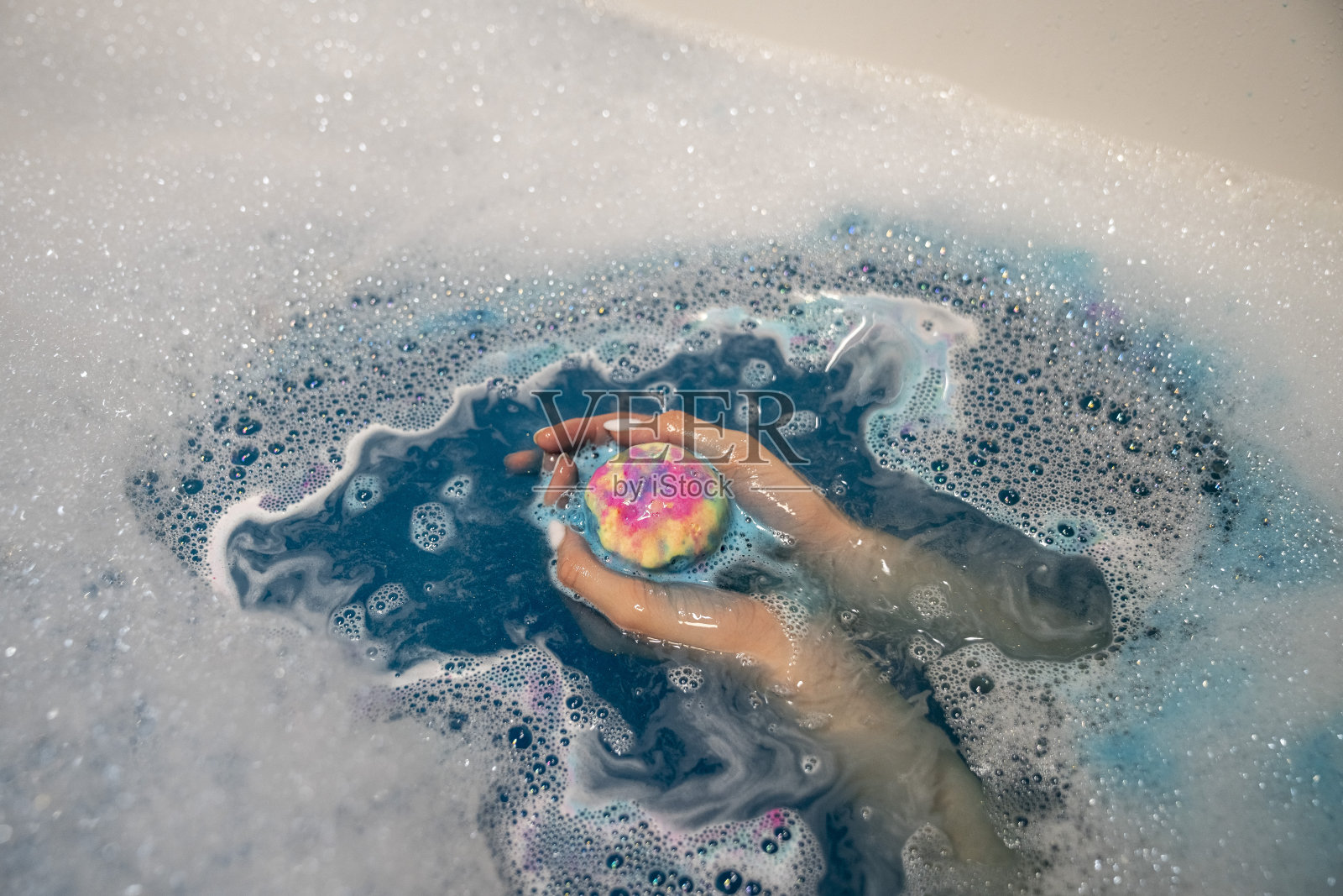 女性的手，水溶性蓝色，黄色，粉色，沐浴炸弹，气泡水，近距离。照片摄影图片