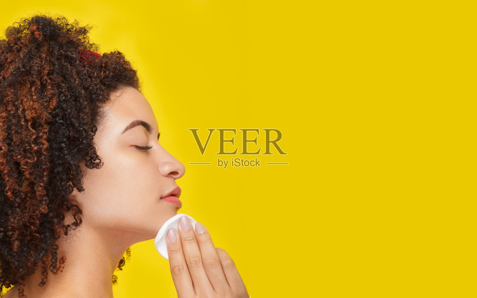 一个闭着眼睛的女人在黄色背景上用棉花洗脸的侧面特写照片摄影图片