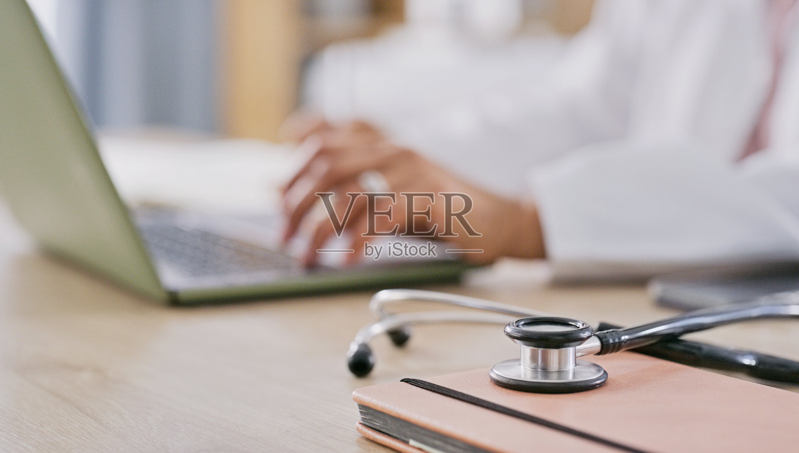 在网上，医生和双手在笔记本电脑上打字进行交流和虚拟咨询。办公室办公桌上的医疗、人员和听诊器特写，配有专家研究、患者信息和报告照片摄影图片