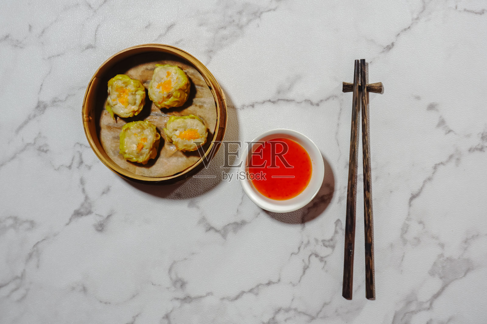 烧麦放在竹篮蒸笼里，蘸酱和筷子放在大理石背景上。平的。照片摄影图片