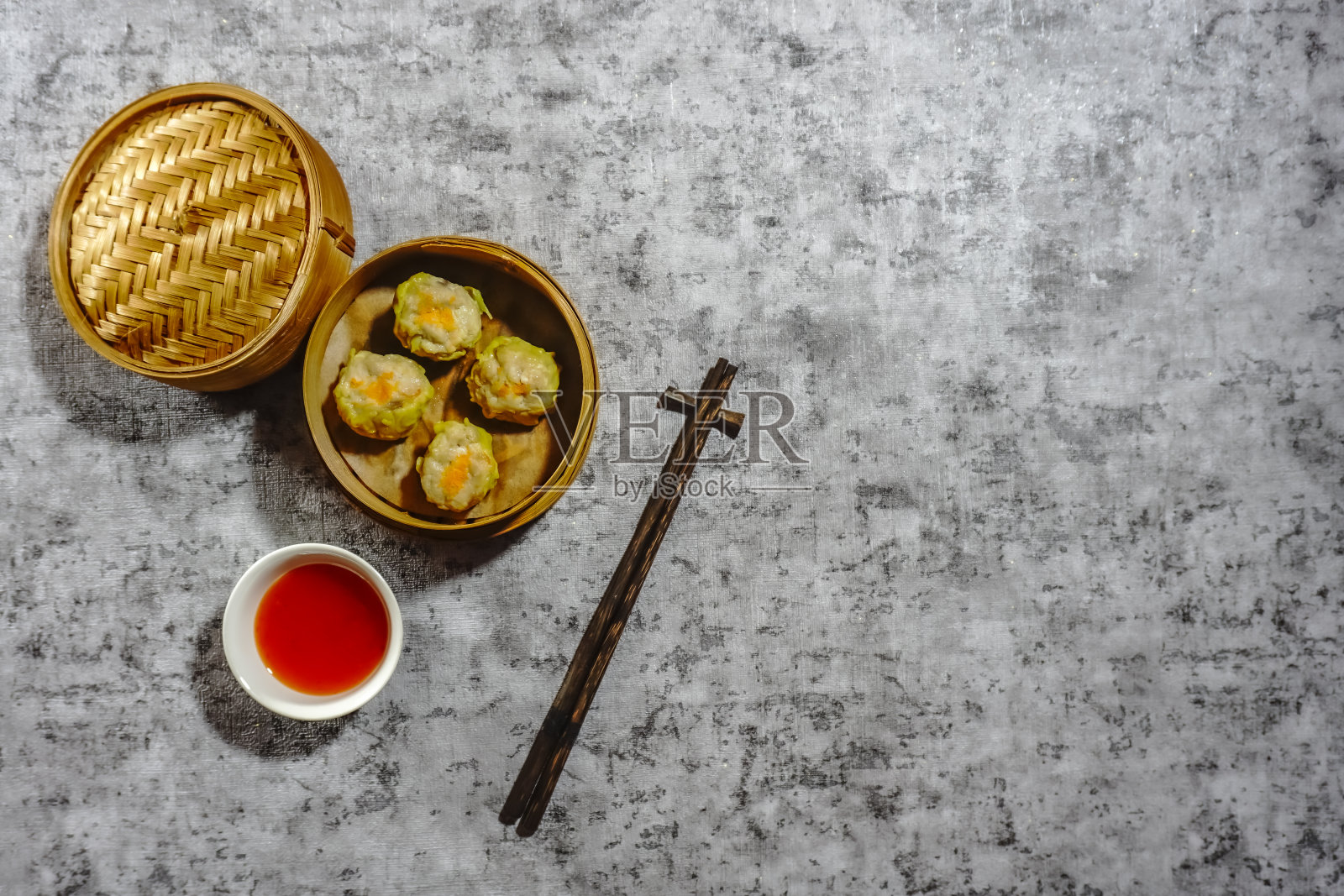 蒸饺烧麦装在竹篮蒸笼里，筷子被隔离在灰色的背景上。平的。本空间照片摄影图片