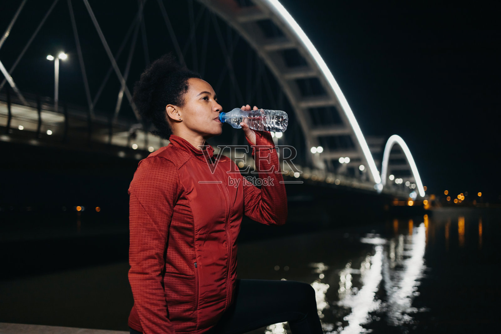 成熟的女运动员在河边喝水照片摄影图片