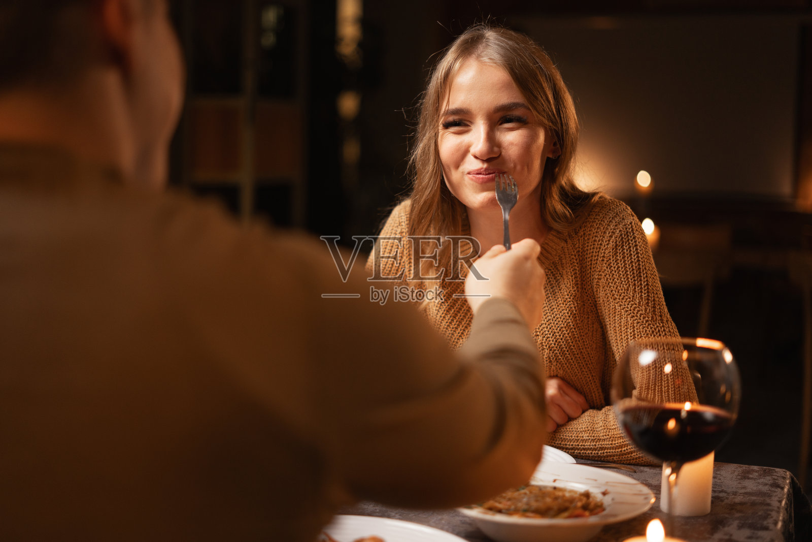 幸福的情侣在餐厅吃浪漫的晚餐，晚上吃吃喝喝，庆祝情人节。有爱的男人用叉子喂他的妻子，一起享受浪漫时光照片摄影图片