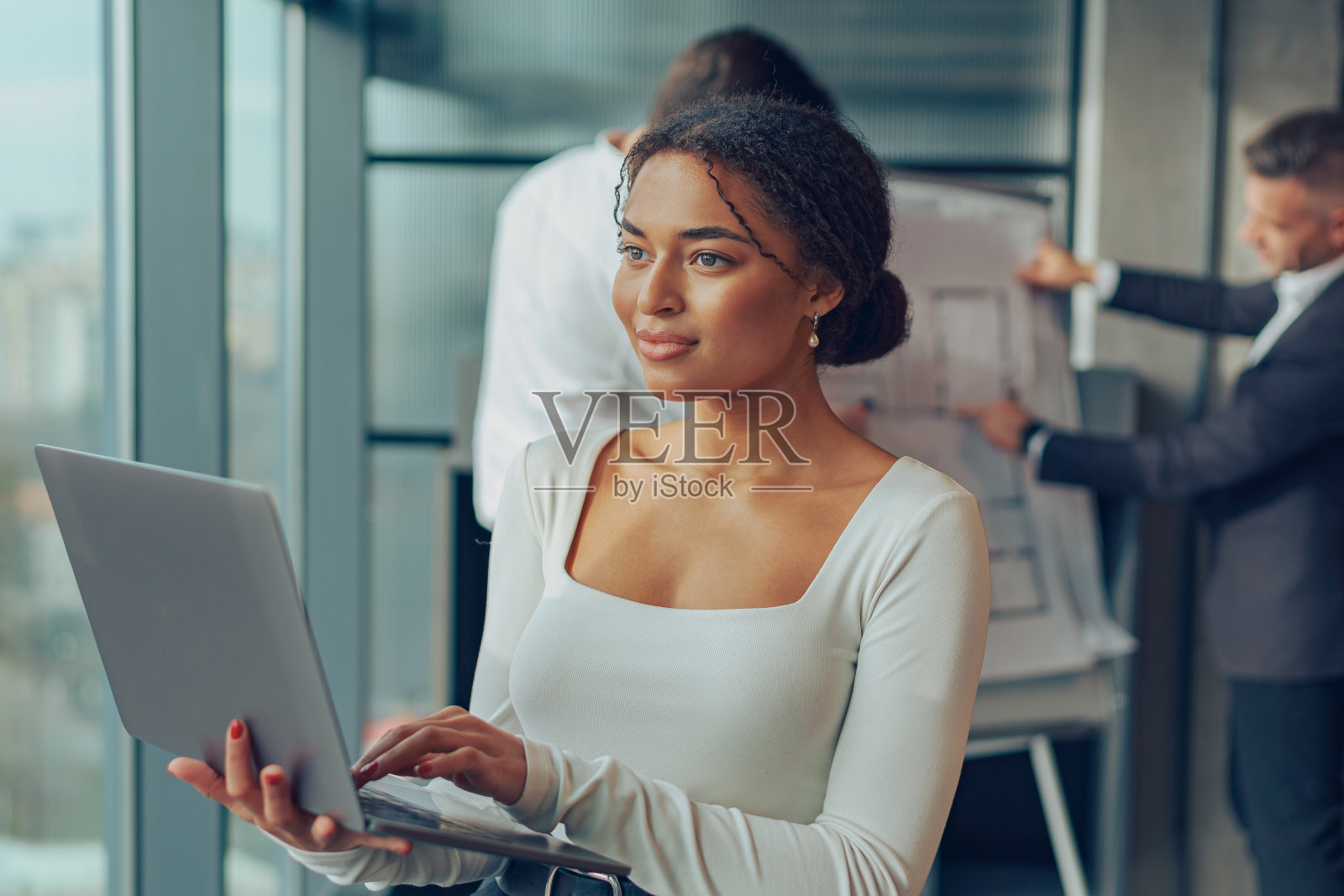 微笑的女经理站在办公室，在同事的背景下摆弄着笔记本电脑照片摄影图片