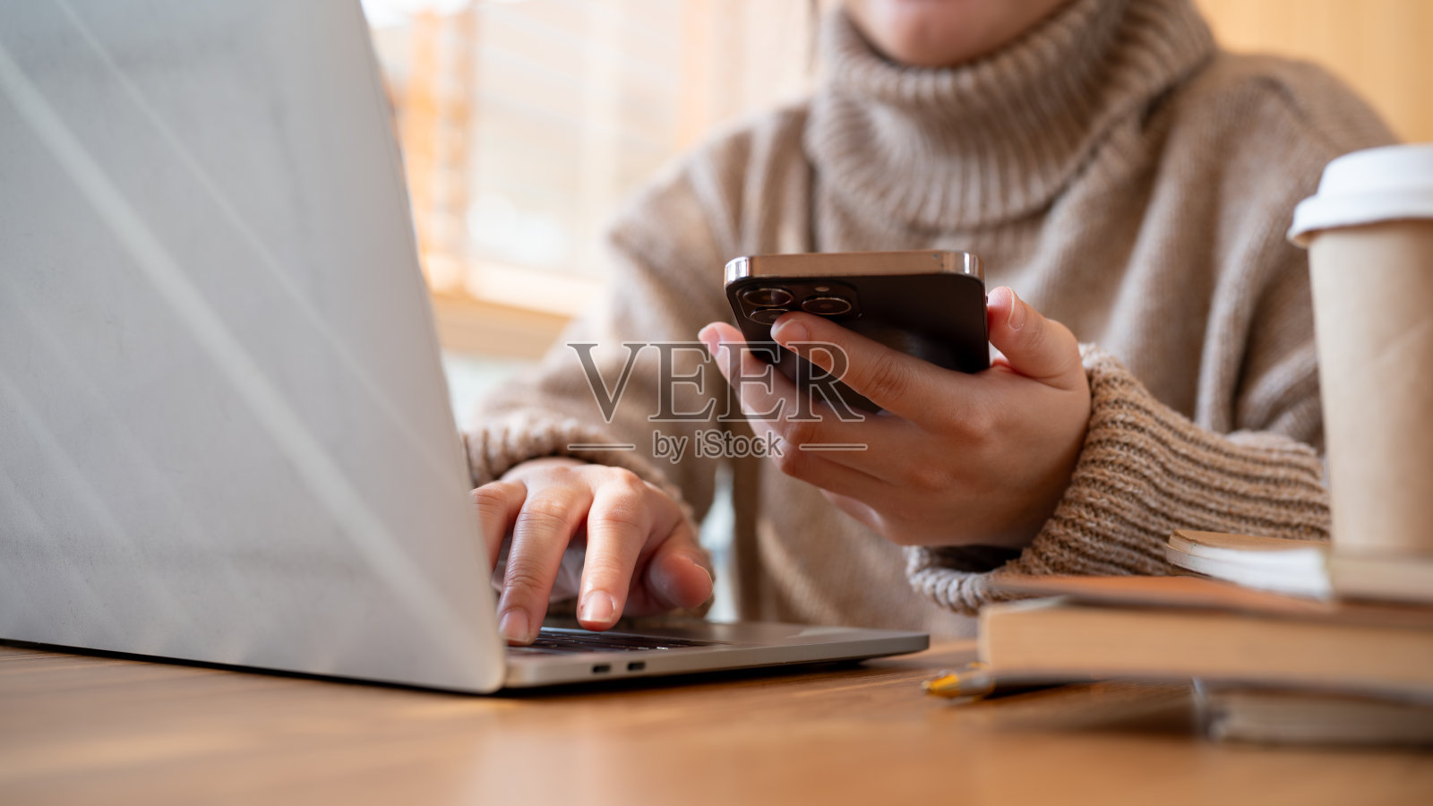 一个女人坐在咖啡馆的桌子上使用她的智能手机和笔记本电脑。照片摄影图片