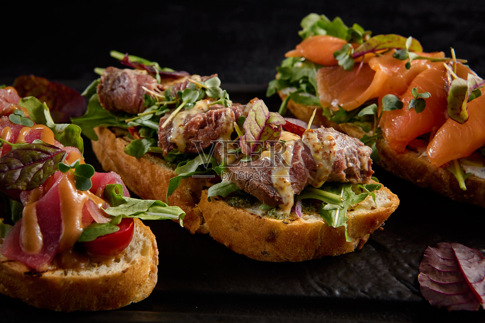 烤面包配鲑鱼，烤牛肉和金枪鱼，放在黑色矩形盘子里照片摄影图片