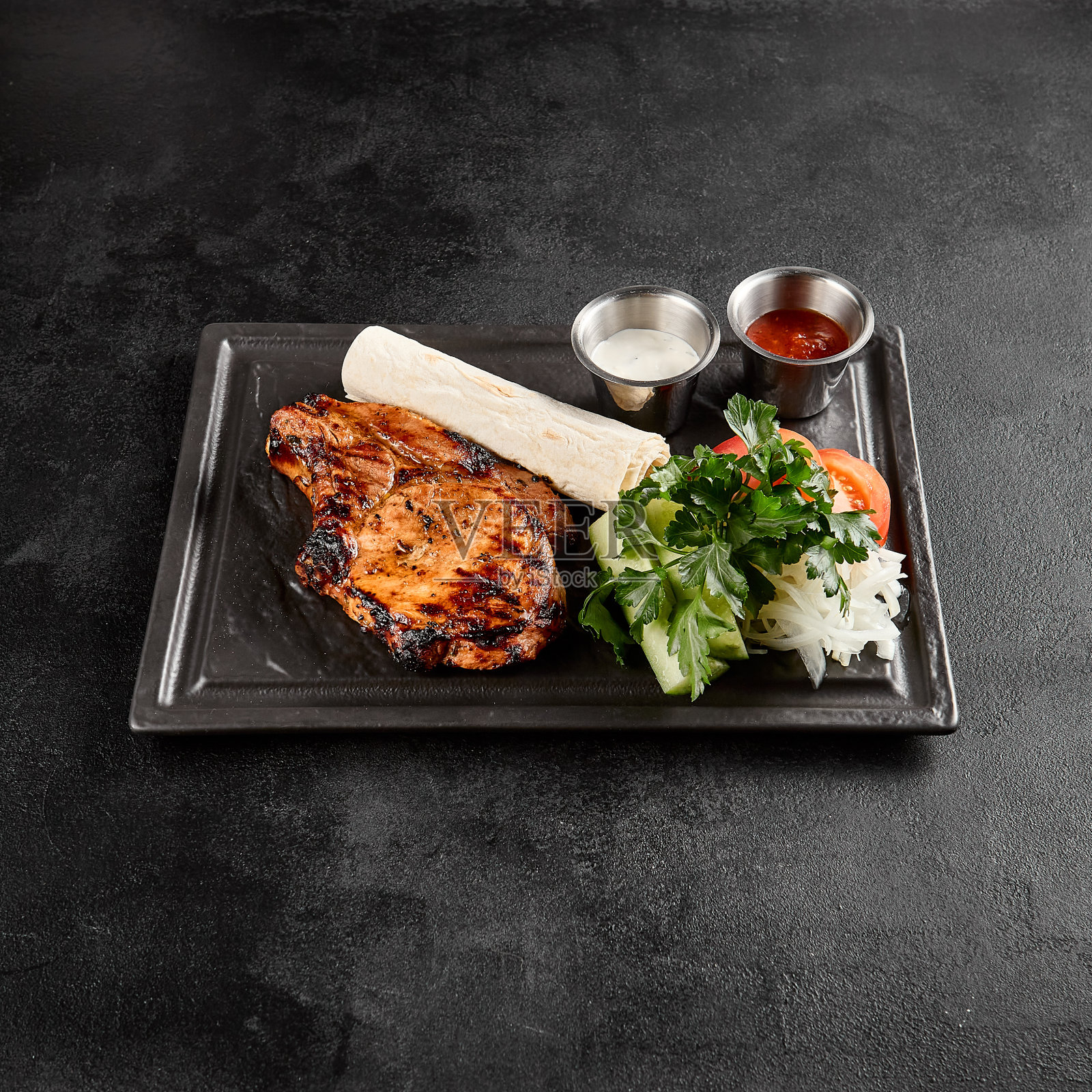 烤猪里脊肉配新鲜蔬菜，lavash，和酱汁在石板盘上照片摄影图片