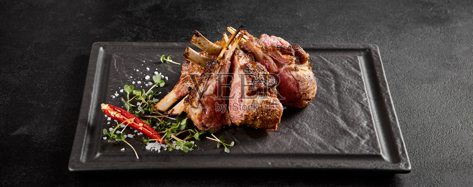 完美的烤羊排装在石板盘上，配上新鲜的香草和辛辣的红辣椒照片摄影图片