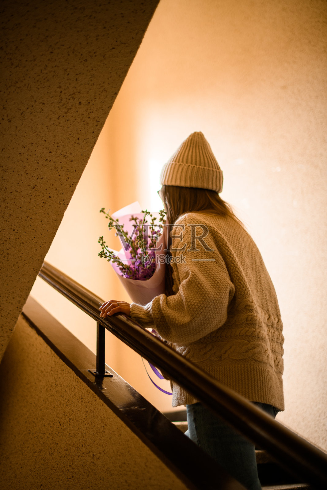 身穿白色针织衫、手捧一束质朴花的黑发女子后视图爬上楼梯照片摄影图片