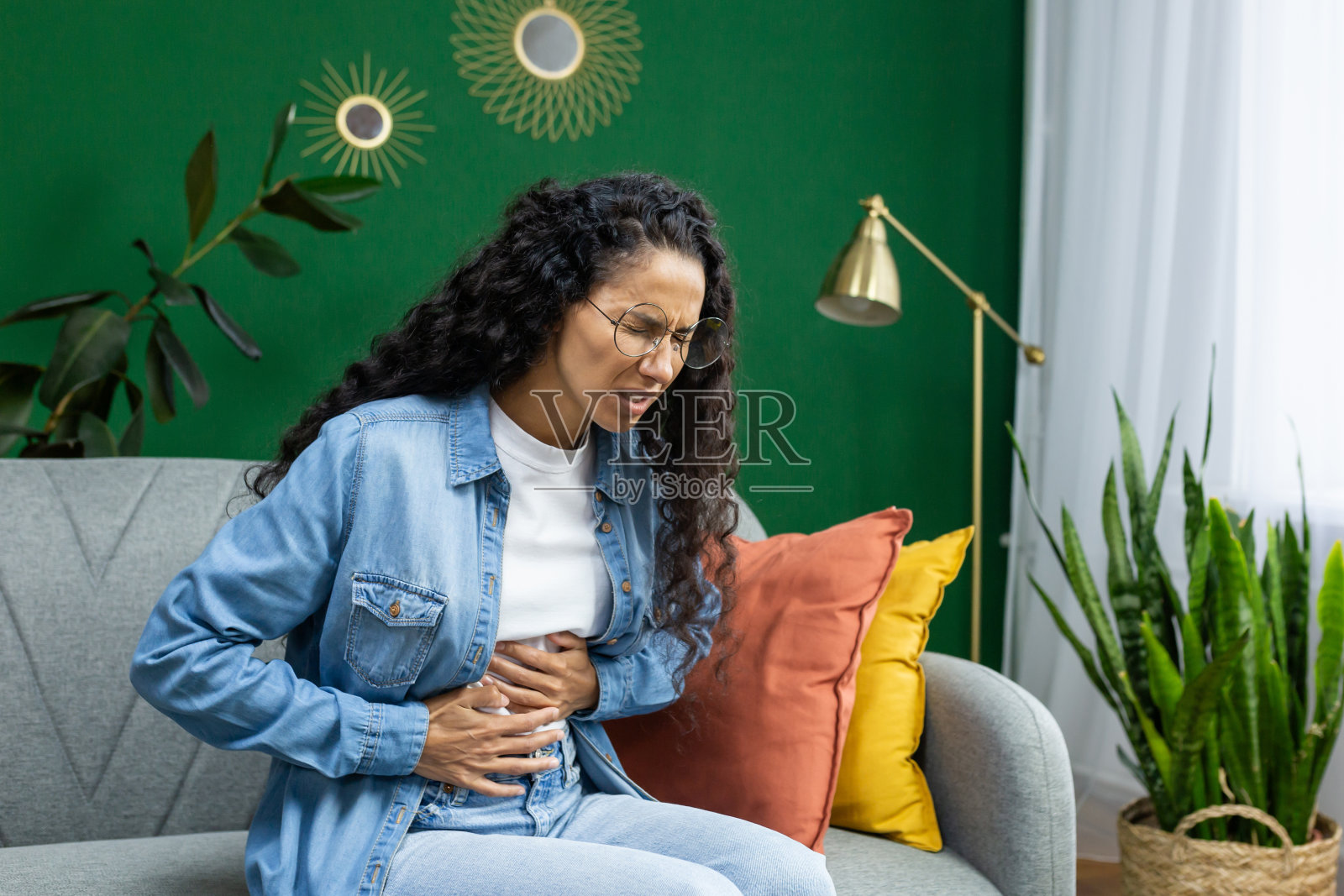 女人坐在沙发上，不舒服地捂着肚子照片摄影图片