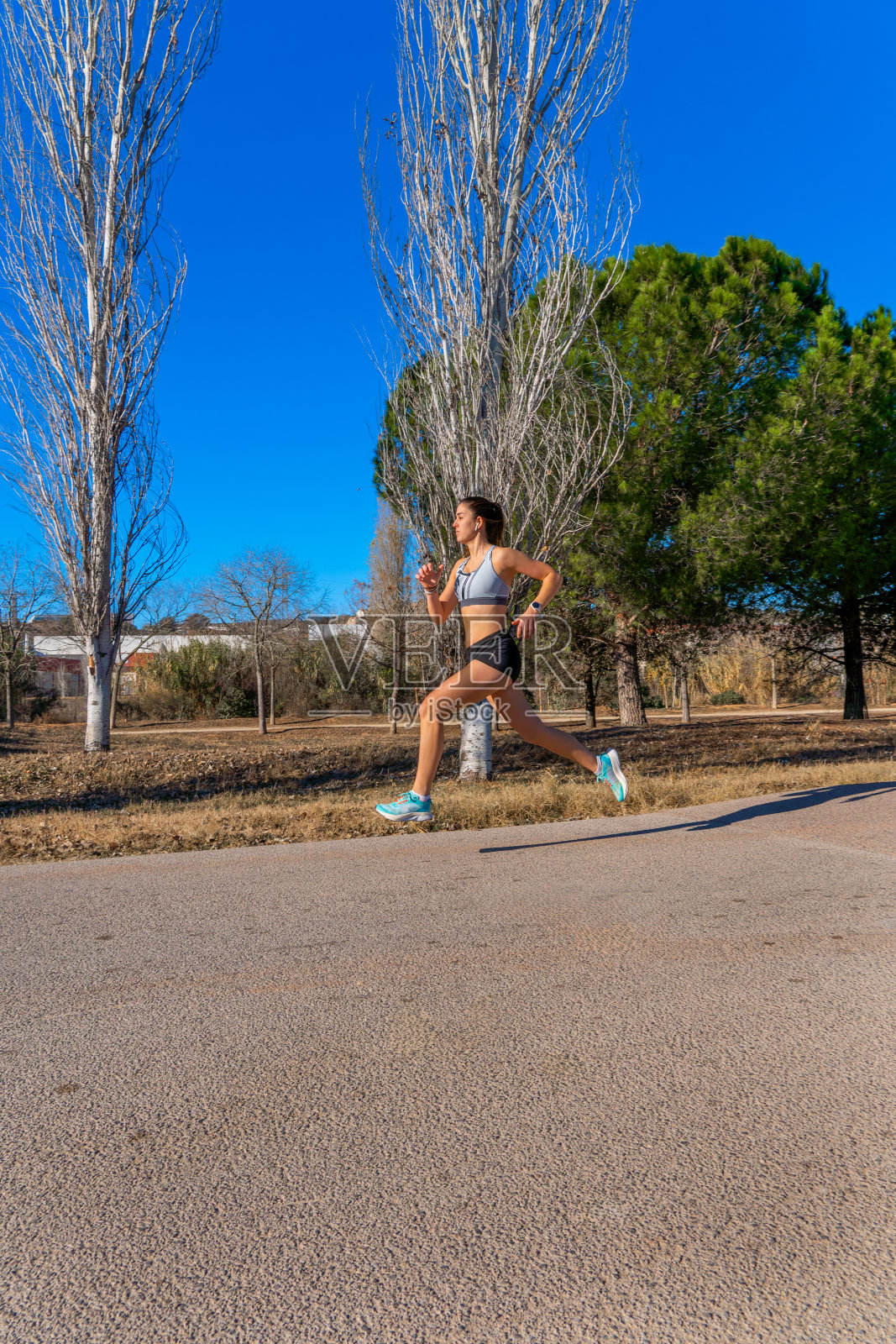 一位年轻的跑步女，穿着紧身短裤和白色上衣，在黎明时分，在山间公园的一条铺好的小路上，以完美的技术，在空中迈着大步跑着。照片摄影图片