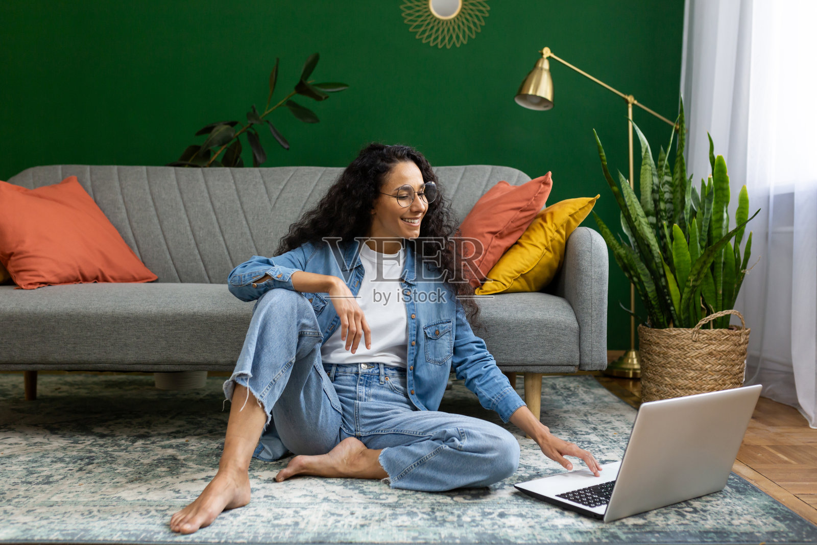 快乐的成功女士远程使用笔记本电脑工作，西班牙裔妇女坐在客厅的地毯上，愉快地敲打键盘照片摄影图片