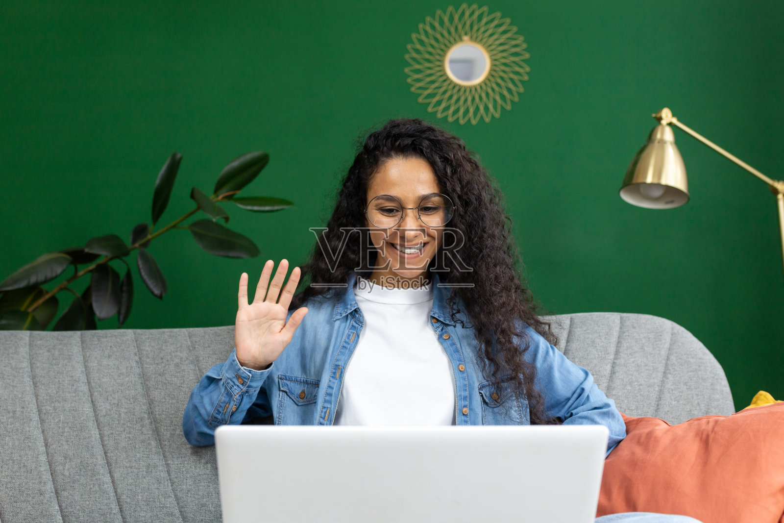 在家中进行视频通话时，戴眼镜的微笑女人在笔记本电脑屏幕上挥手，家居装饰时尚照片摄影图片