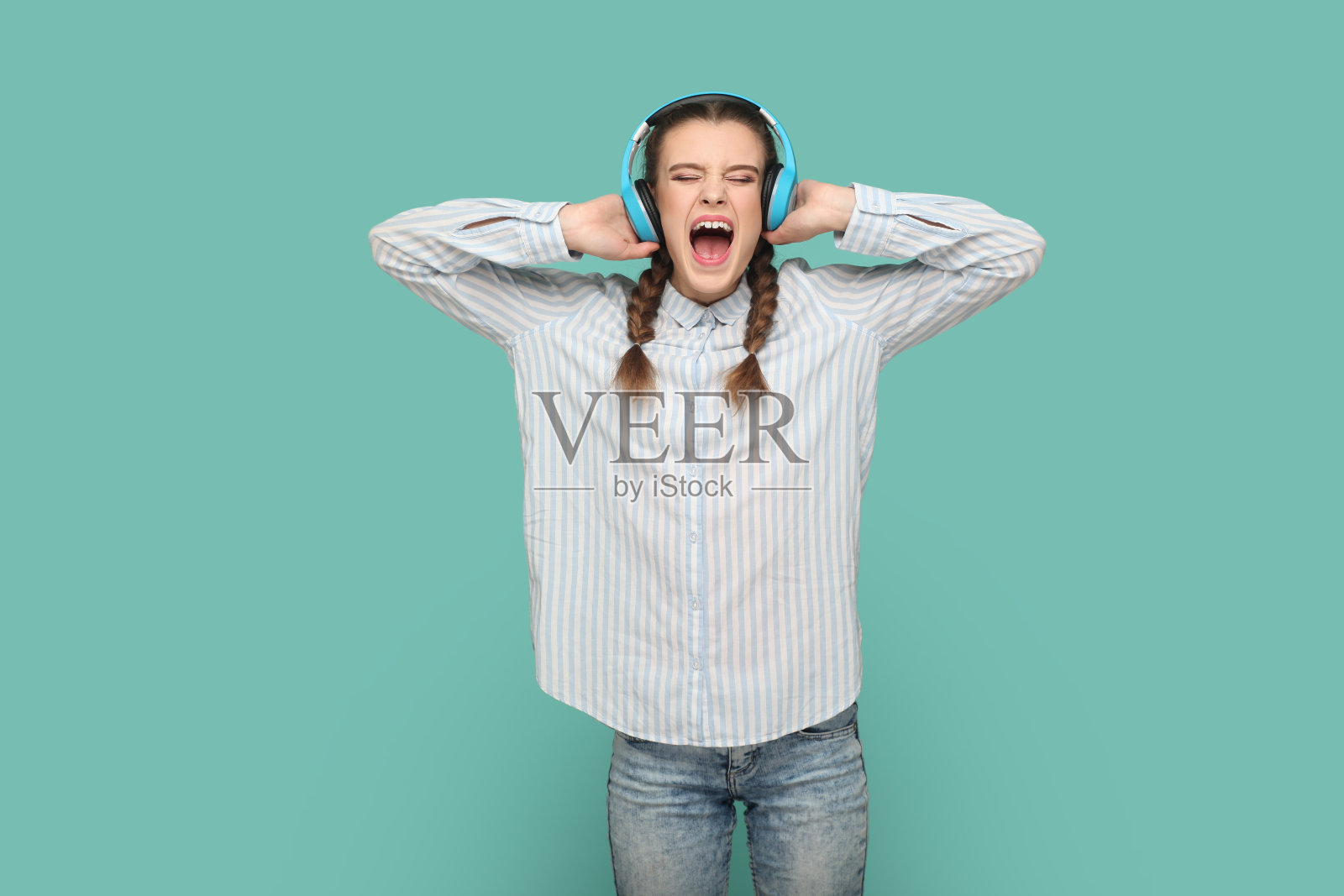 兴奋疯狂的女孩站着，戴着耳机听着喜欢的音乐，张大嘴巴唱歌。照片摄影图片