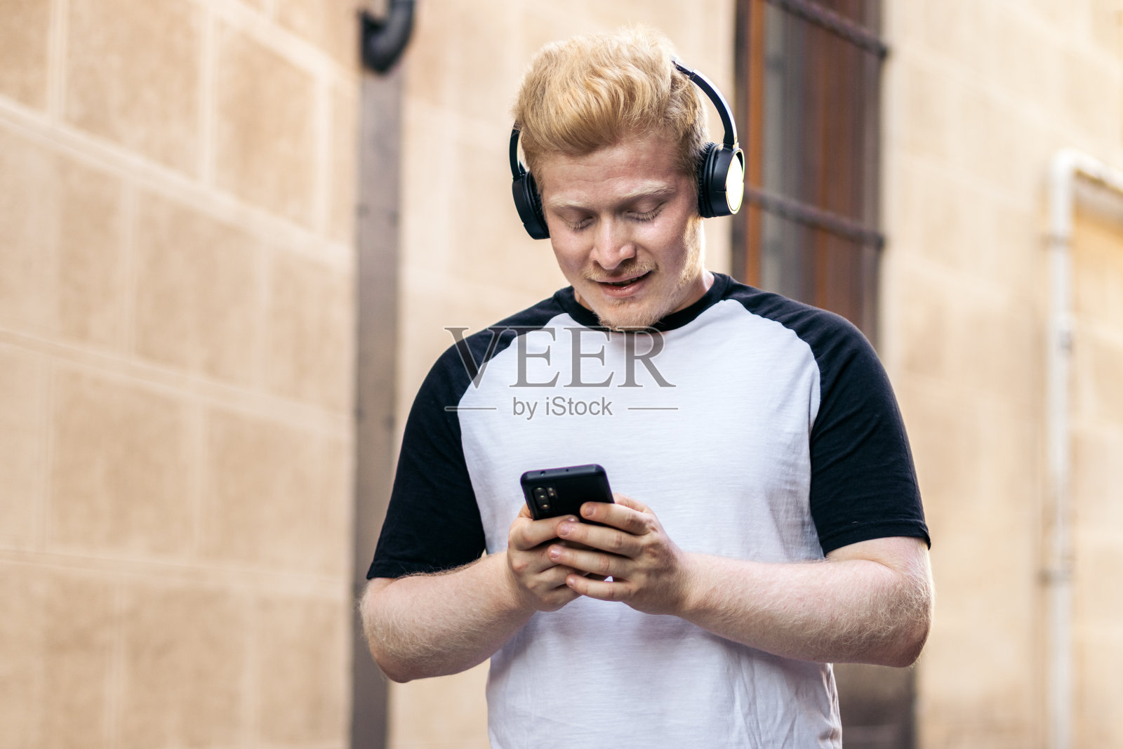 白化病患者一边用智能手机走在街上，一边戴着耳机听音乐照片摄影图片