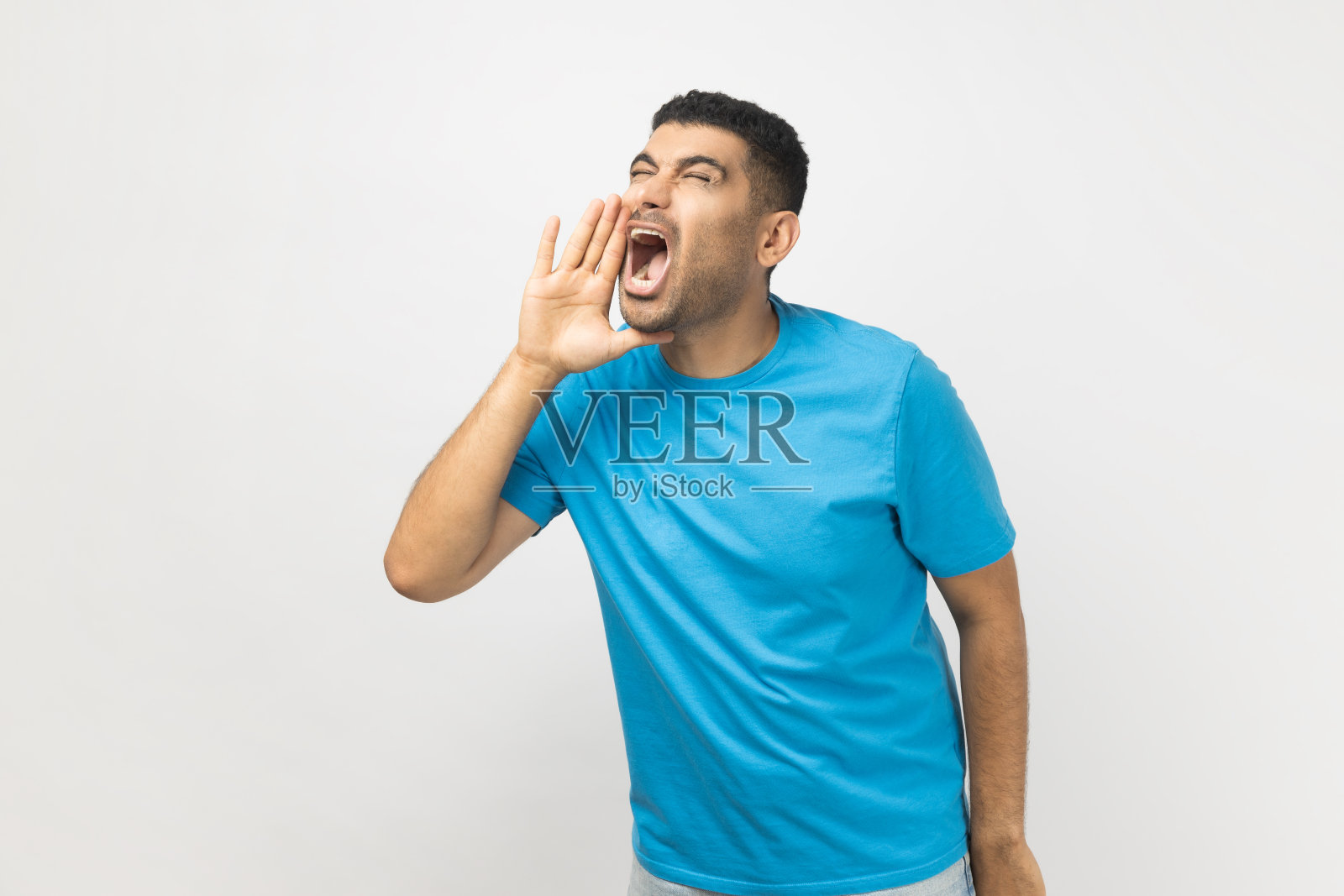 穿着蓝色T恤的兴奋的未刮胡子男人张着嘴，大声喊着新闻照片摄影图片