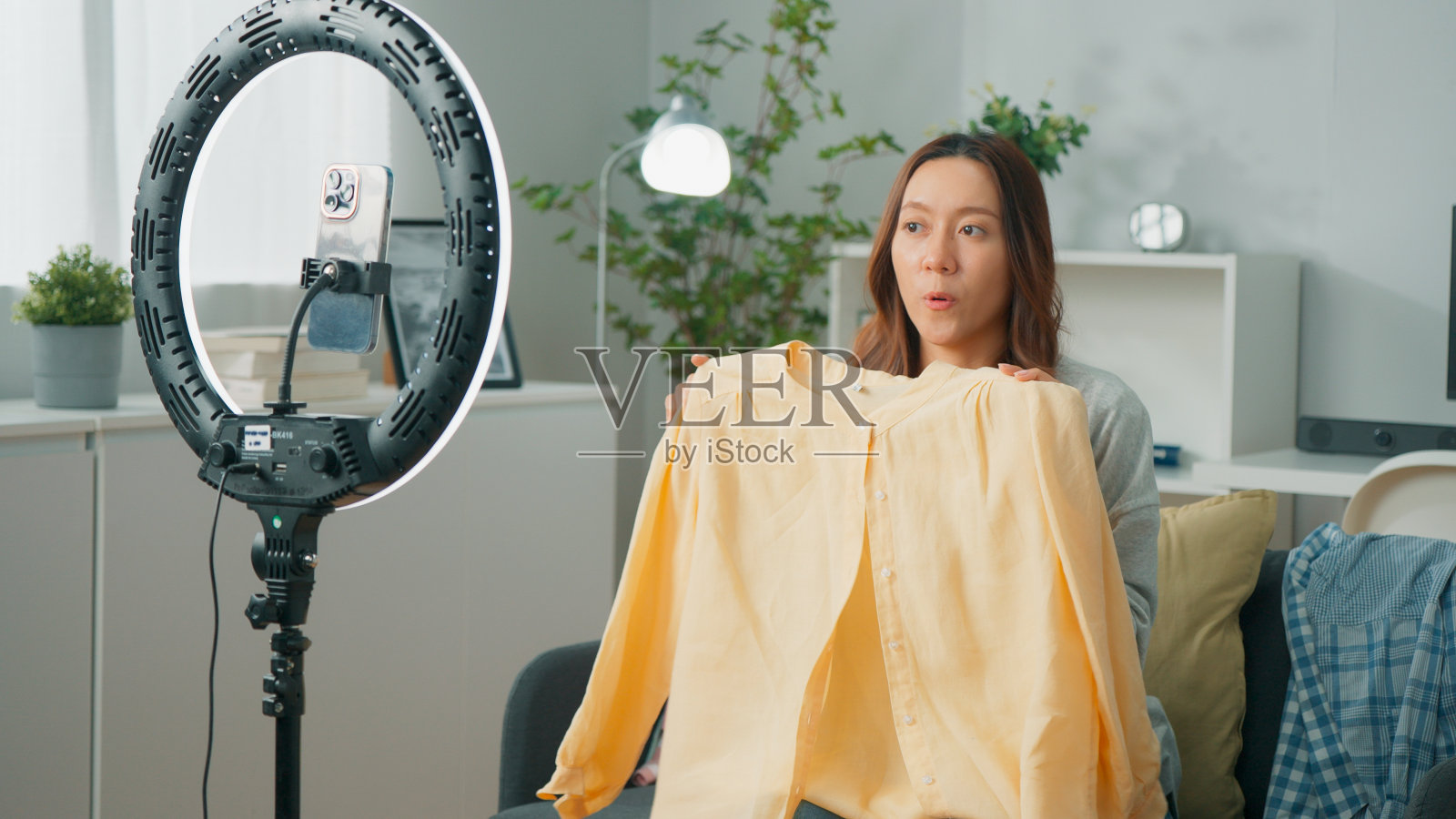 有吸引力的年轻亚洲女性在线卖家或零售店主使用手机直播，销售服装，并在家里的客厅通过互联网与观众在线交谈，快乐的女性利用技术开展业务照片摄影图片