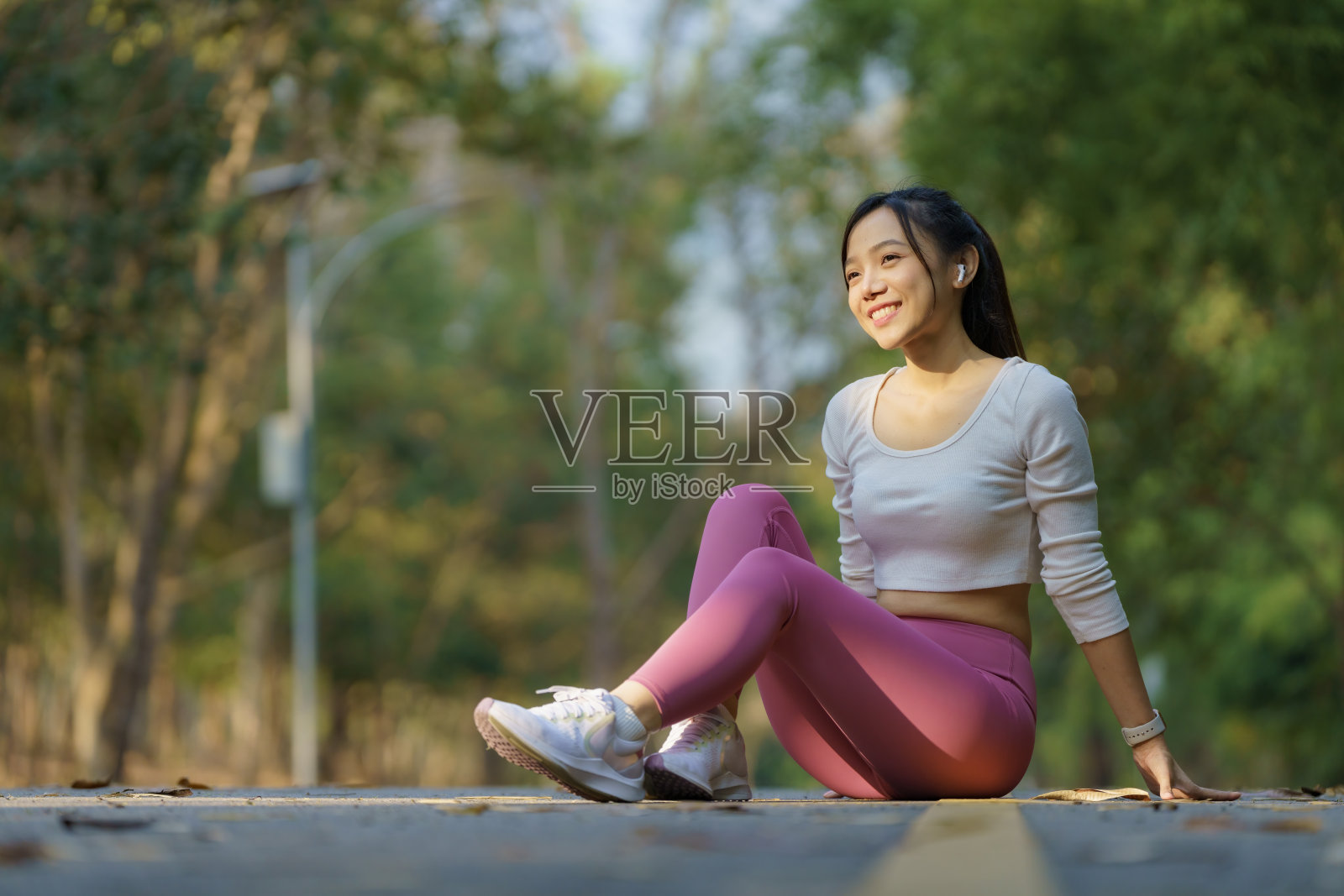 一位亚洲妇女坐在人行道上，享受着在公园跑步后应得的休息。照片摄影图片