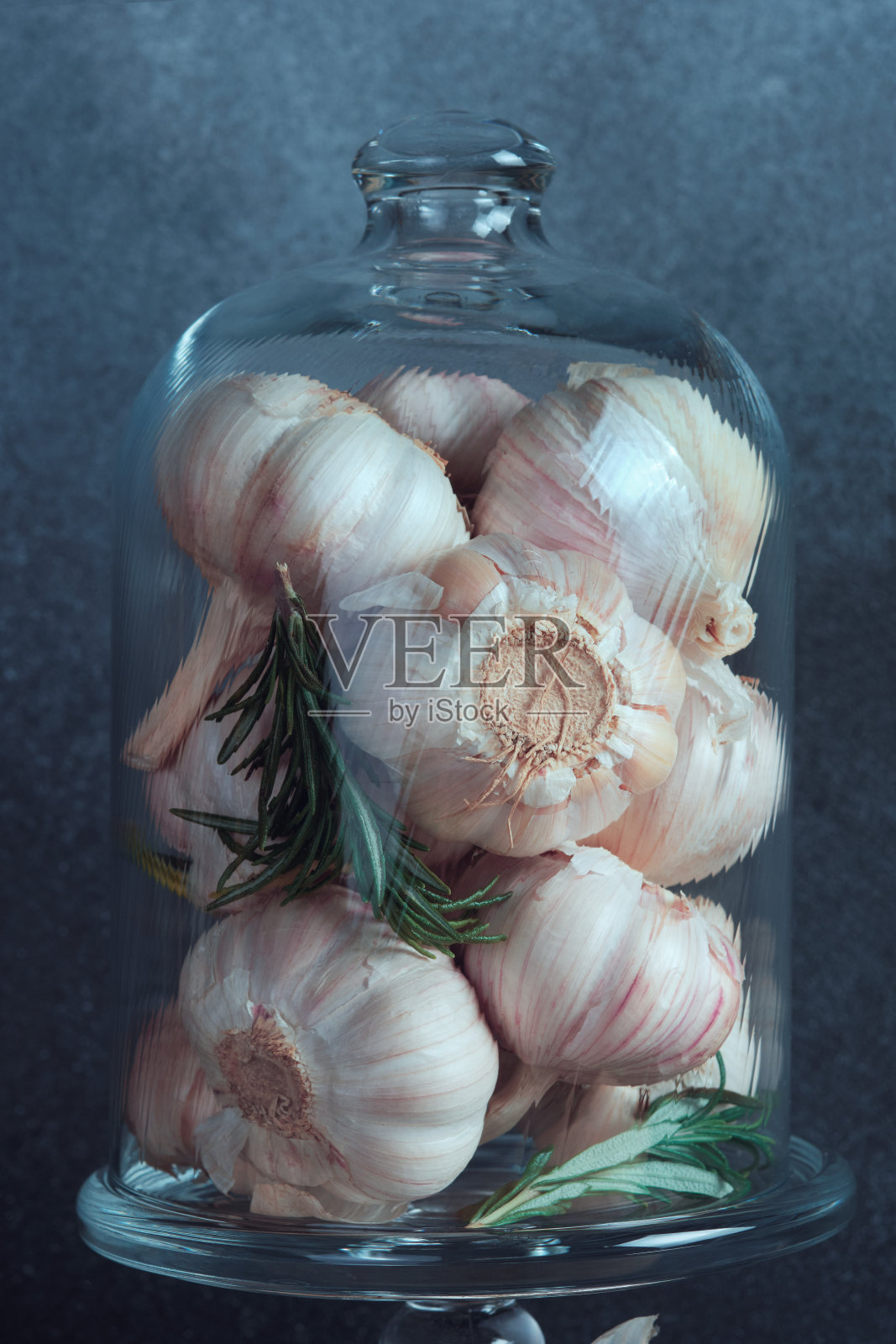大蒜球茎优雅地陈列在玻璃钟里。用迷迭香装饰的透明玻璃钟形花瓶里陈列着各种各样的蒜头。照片摄影图片