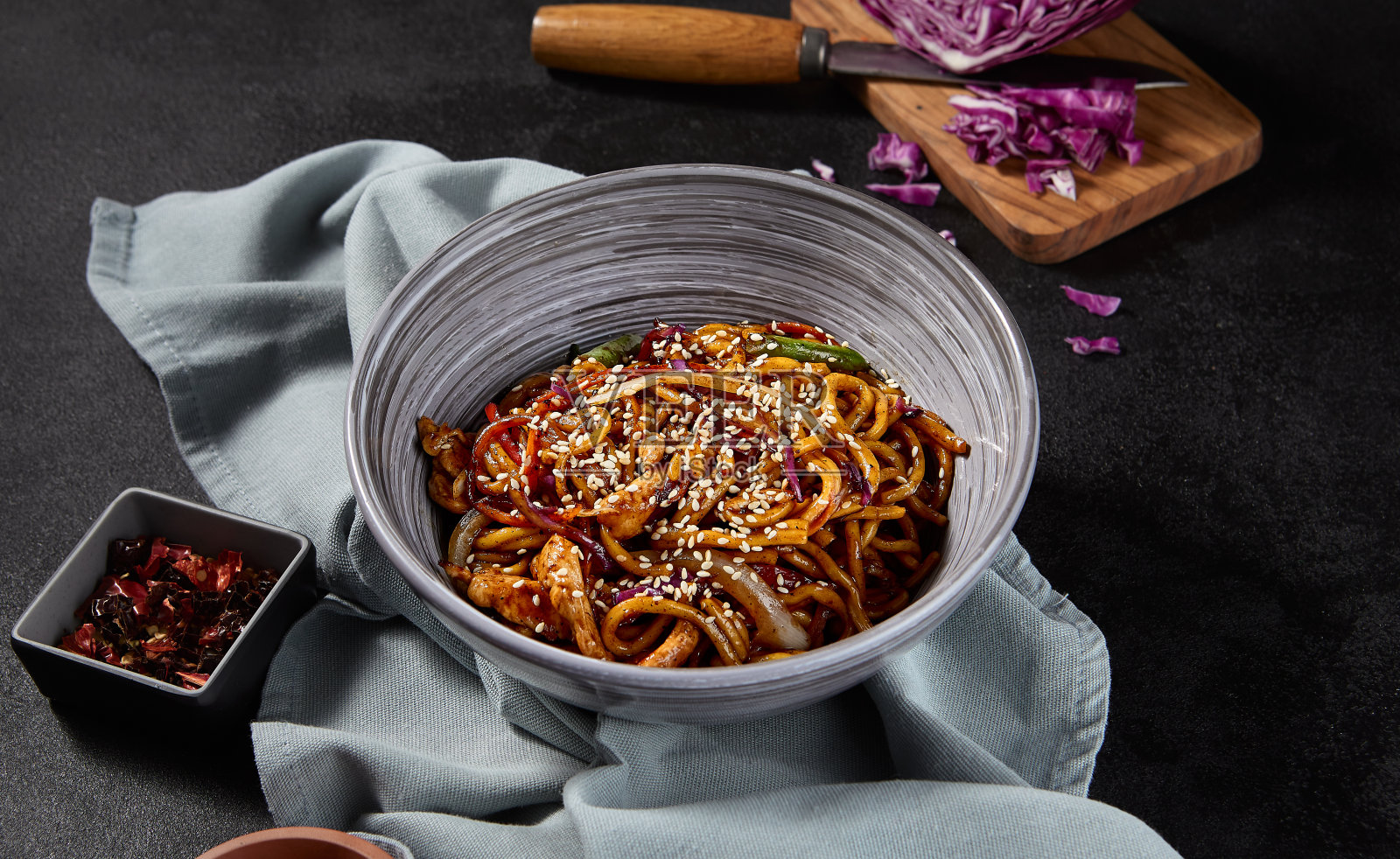 侧视图，水平镜头，一个美味的乌冬菜与鸡肉和蔬菜在美味的大蒜酱炒。筷子和有质感的布料与黑色背景相得益彰照片摄影图片