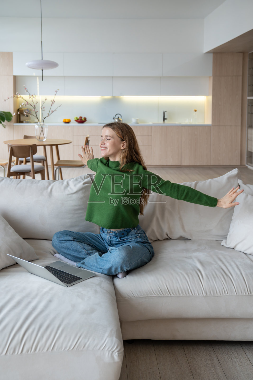 快乐的女人坐在床上，满意地伸开双臂，结束了在线工作和教育照片摄影图片