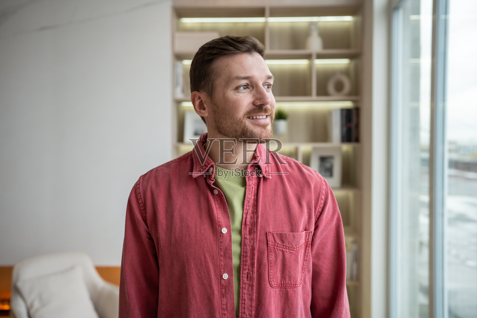 微笑着放松的男人看着新房的窗户，想着未来，做着白日梦。照片摄影图片