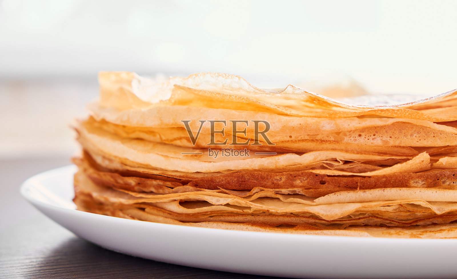 一个圆形的盘子，上面放着煎薄饼，放在棕色的桌子上。早餐吃甜点。阳光明媚的早晨。照片摄影图片