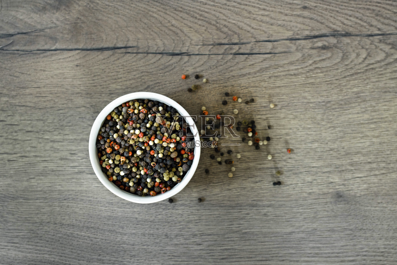 木制背景上的白色盘子上混合着各种辣椒和豌豆。成堆的各种辣椒。红色，黑色和白色胡椒子的混合，分离在白色上。俯视图照片摄影图片