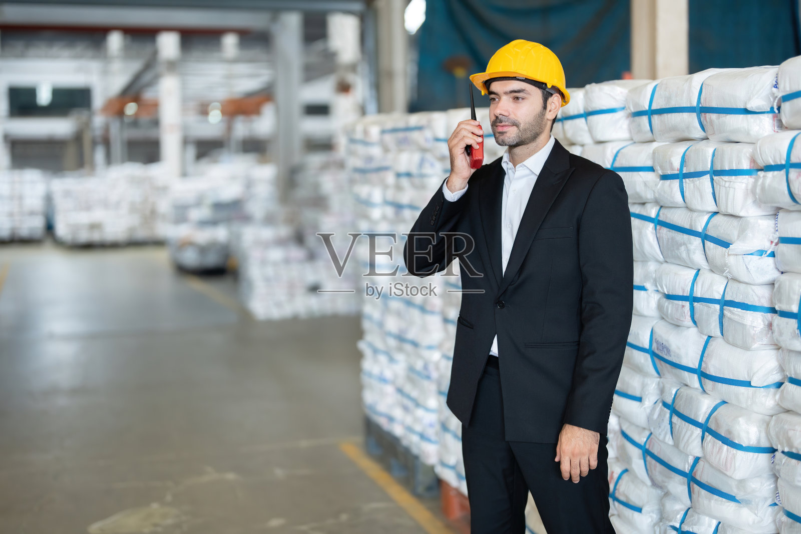 美国男工程师在广播中谈论塑料和钢铁工业的出口业务。戴安全帽，穿工作服。后面是准备送到商店的产品。照片摄影图片