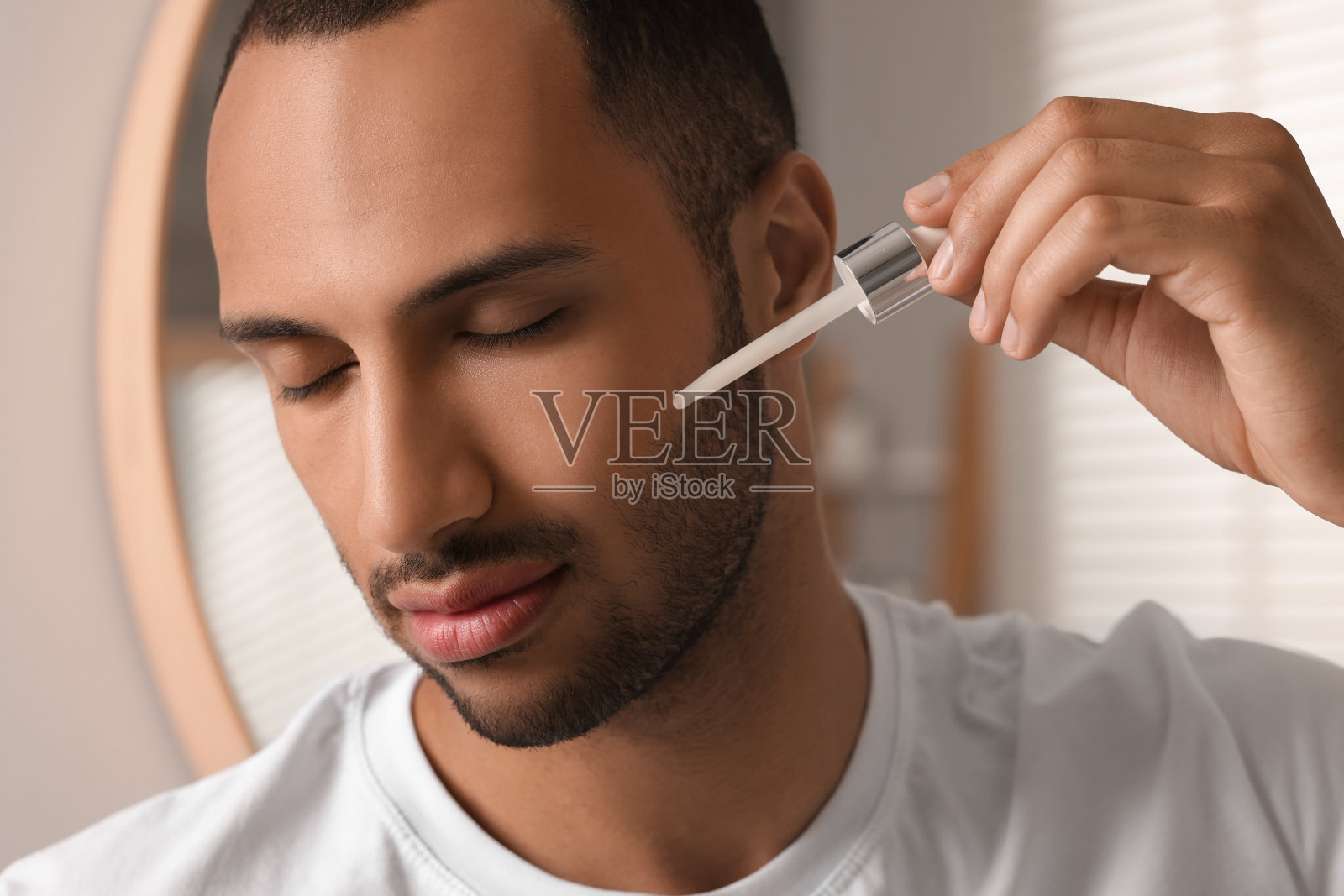 一个帅哥在室内给脸上涂化妆品精华液，特写照片摄影图片