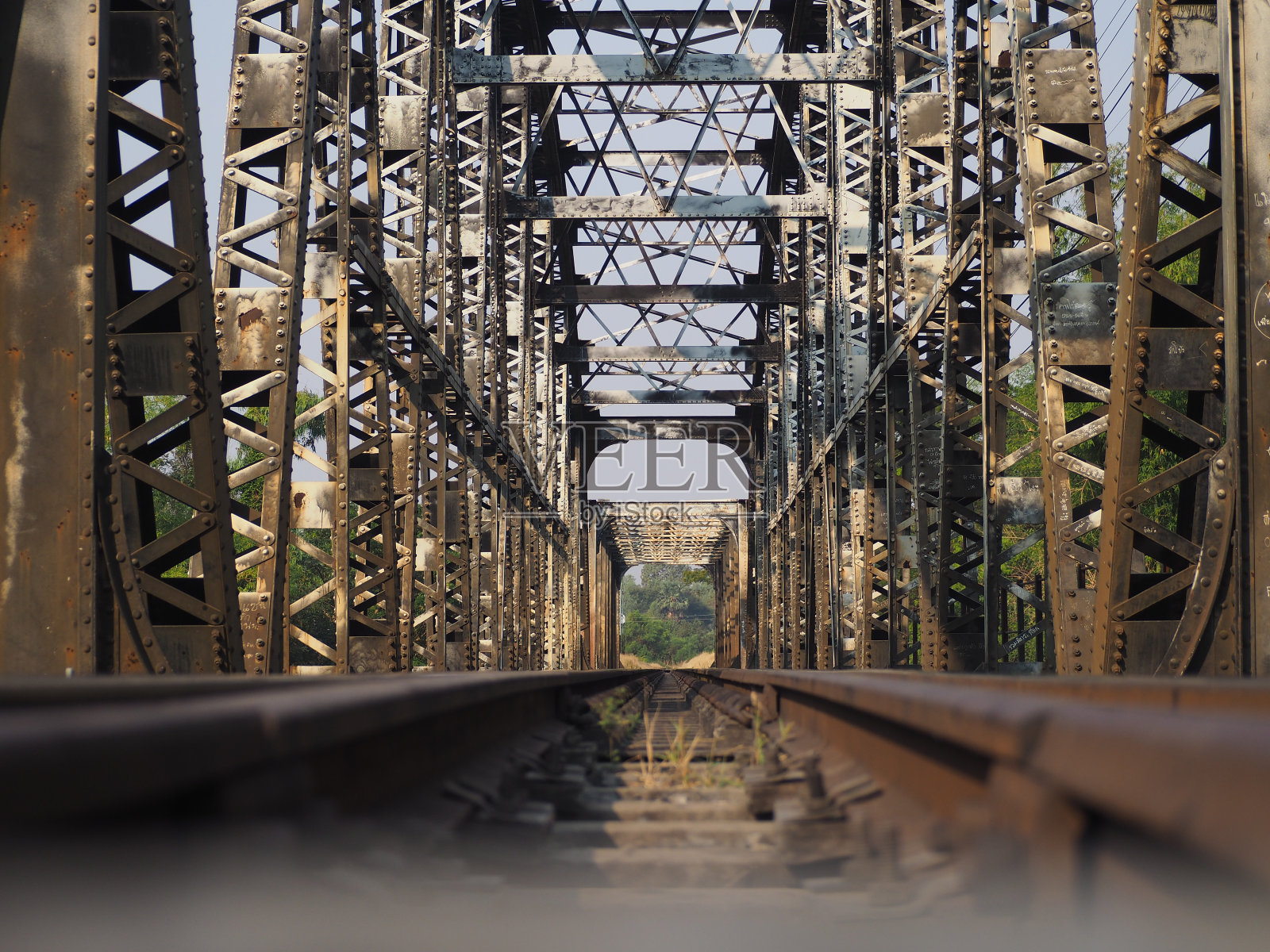 灰色、黄色、黑色和棕色的钢架和柱子，绿色的树叶和水渠，蔚蓝的天空。照片摄影图片